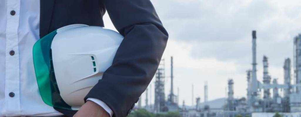 refinery engineer with white safety helmet see drawing standing in front of oil refinery building structure in heavy petrochemical refinery industry.